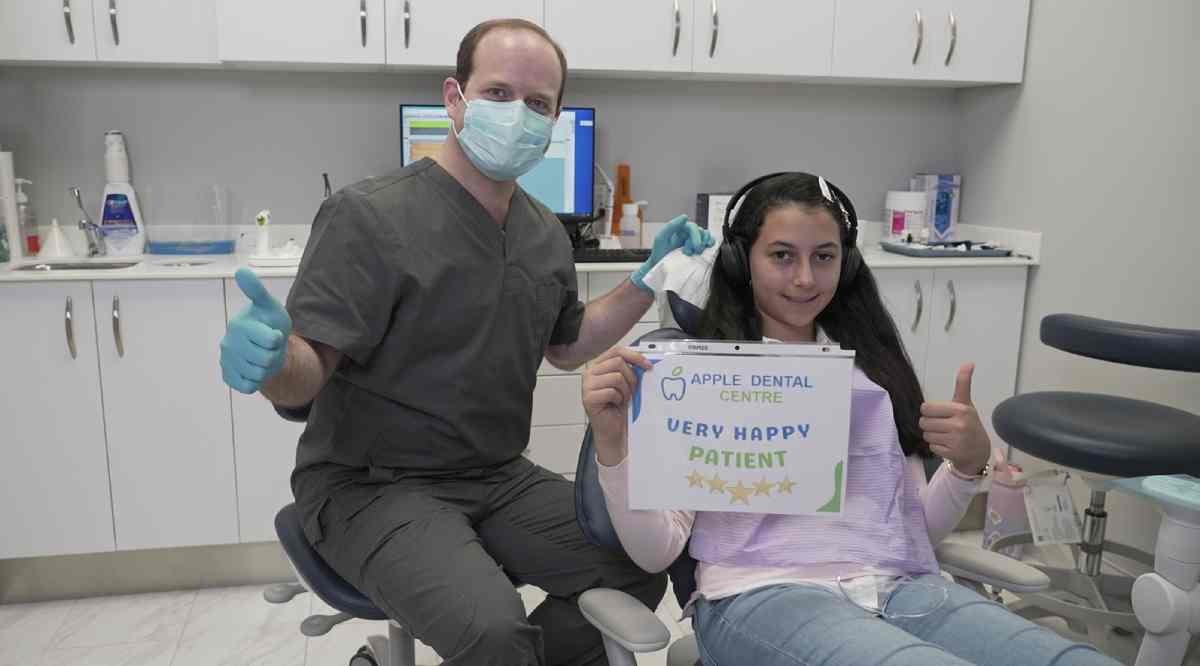 Dr. Subhi Alnahas poses with a young patient who is holding up a sign that reads 'Very Happy Patient' with 5 stars. Both the doctor and the patient are giving enthusiastic thumbs up gestures, and they are smiling warmly.